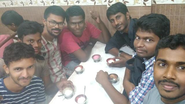 A bunch of 7 people crowded together in a small table eating icecream and looking at the camera for the photo
